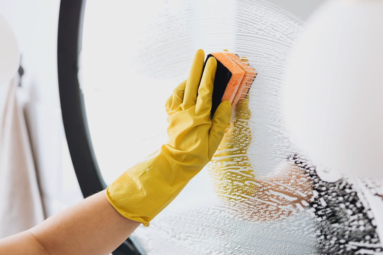 Faceless person cleaning mirror with sponge